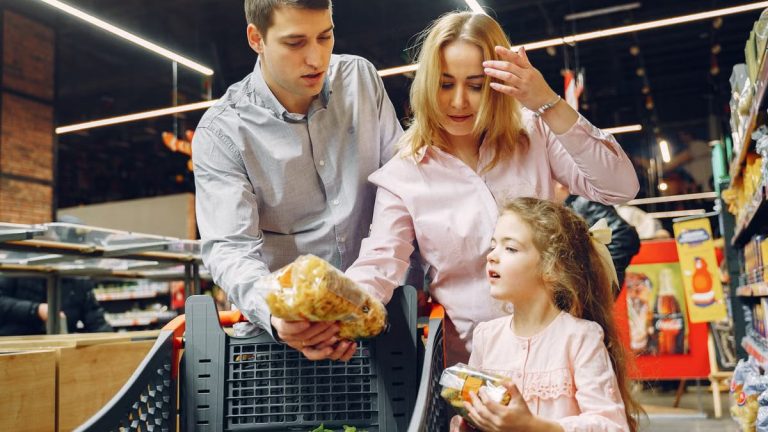 A family enjoying shopping in a supermarket aisle, selecting groceries with a cart.
